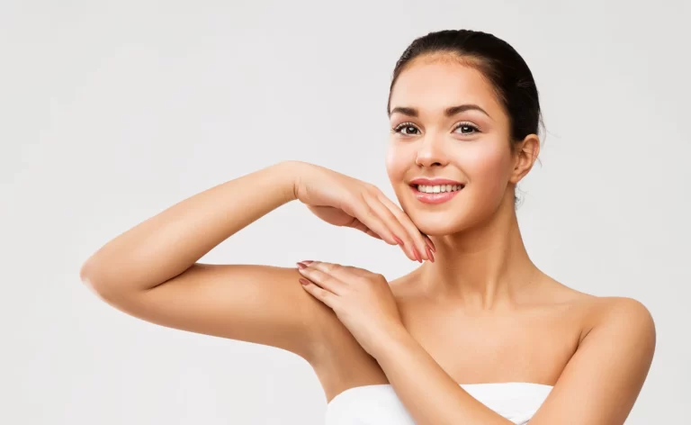A confident woman in a white towel posing with her hand on her shoulder, showcasing the results of Arm Liposuction