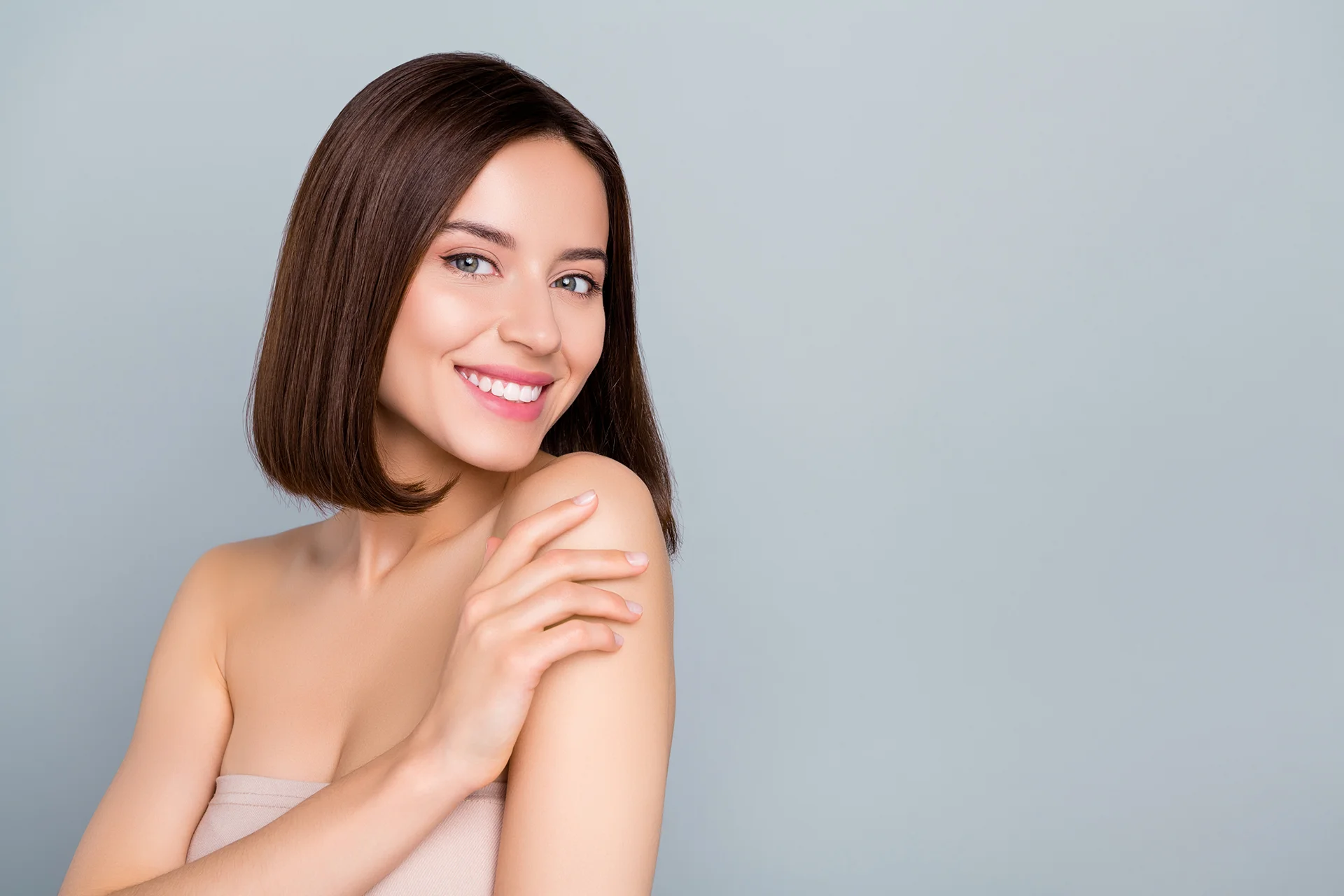A beautiful young woman gracefully posing with her hand on her shoulder.