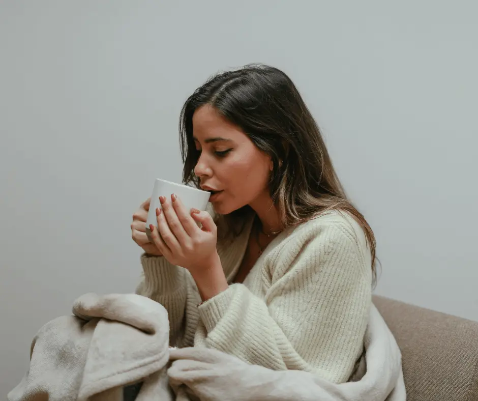 A woman sitting on a couch, casually sipping her coffee.