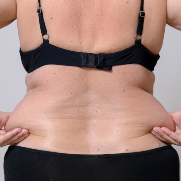 A woman in a black bikini showcasing her toned physique while gracefully placing her hands on her stomach.