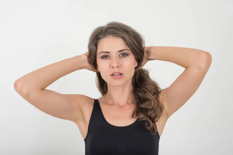 A young woman with sculpted arms, her hands resting on her head.