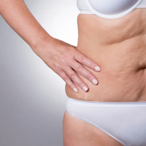 A woman in a white bikini gently resting her hand on her stomach.