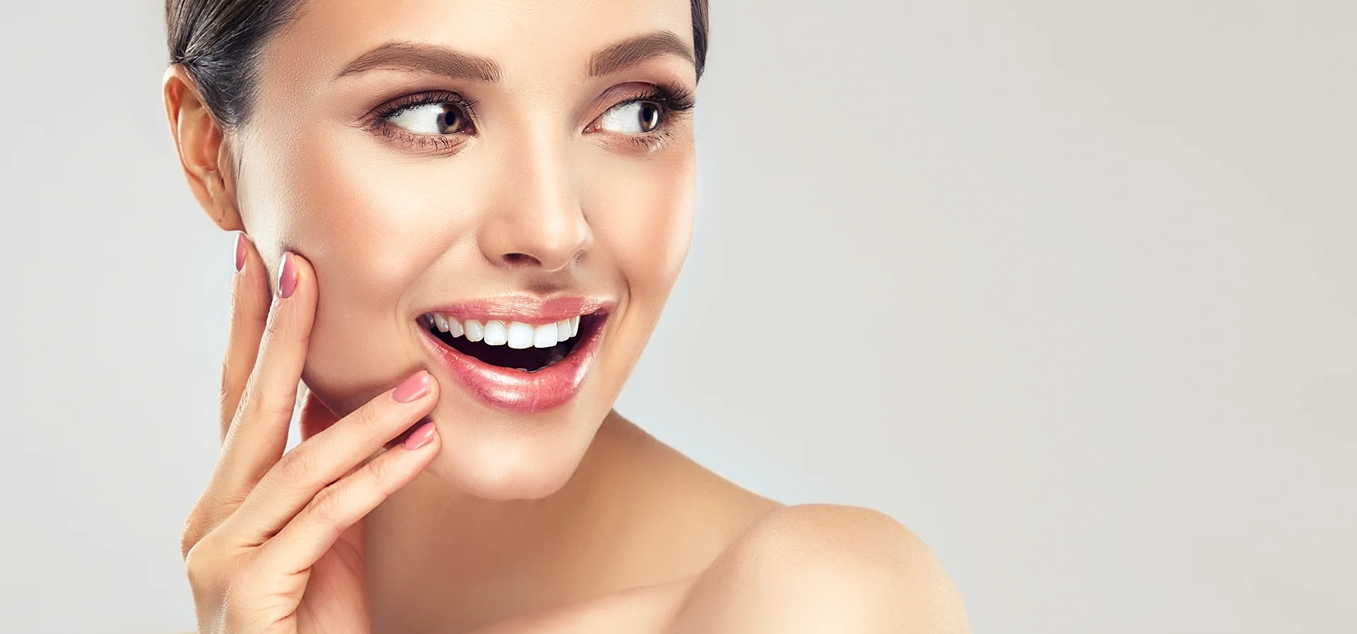 A woman with a beaming smile and her hands resting on her face, showcasing her happiness after smart lipo chin procedure.