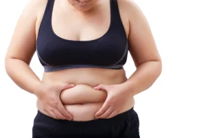 Woman pinching stomach fat, wearing a sports bra and workout pants, isolated on a white background. What You Need to Know about Lipo 360.