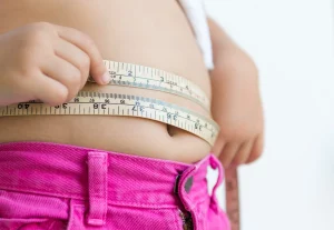 A person measuring their waist with a measuring tape, while wearing bright pink pants and considering Lipo 360 Cost.