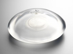 A transparent silicone breast implant is shown on a plain, light-colored surface.