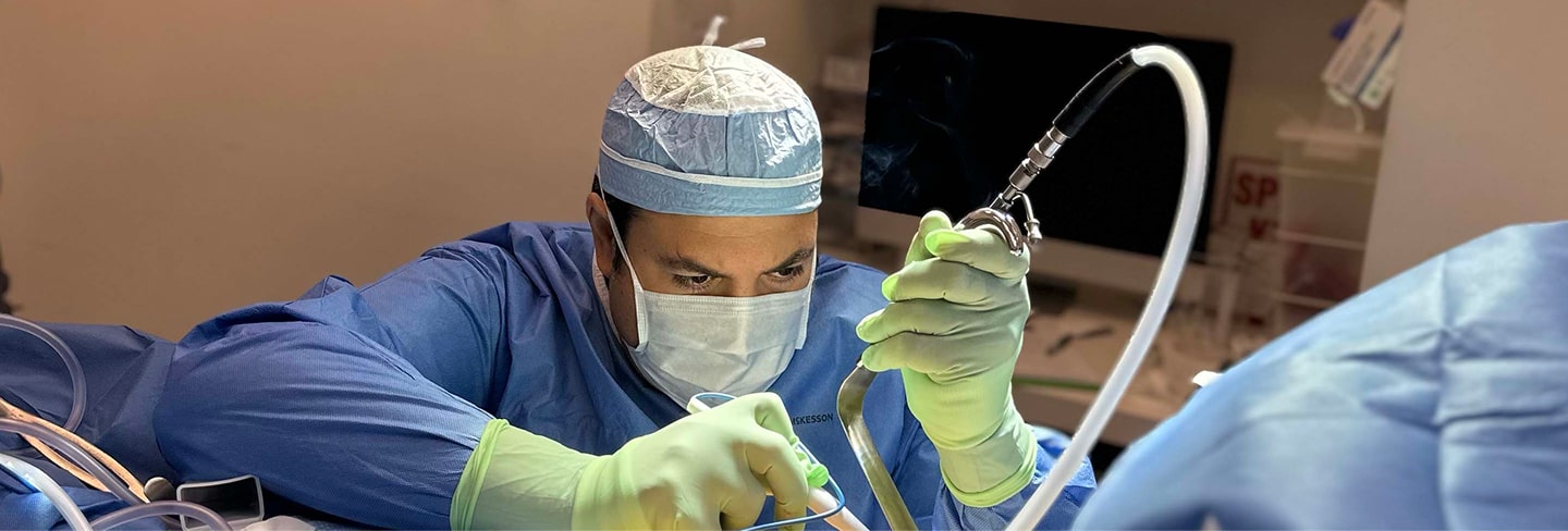 A surgeon in scrubs, mask, and gloves performing a medical procedure using surgical instruments in an operating room.