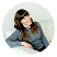 A woman with long brown hair, wearing a gray sweater, sits on a white couch and smiles at the camera in Dr. Darren Smith’s welcoming office.