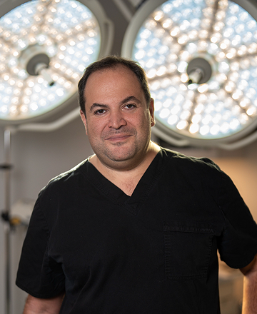 A man in black medical scrubs stands in front of two illuminated surgical lights in an operating room featuring a sleek, modern layout reminiscent of a New Home 2026 design.