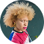 Person with light skin and blonde afro hair wearing a colorful shirt, hoop earrings, and bright lipstick, looking slightly to the side against a dark green background, as seen in rave reviews and glowing testimonials.
