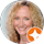 A woman with curly blonde hair smiles at the camera, sharing her positive reviews. An orange and white circular icon is in the lower right corner of the image.