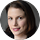 A woman with straight brown hair and light skin is shown in a close-up portrait, looking at the camera with a slight smile. The dark, blurred background gives the photo a professional feel, making it ideal for reviews or testimonials.