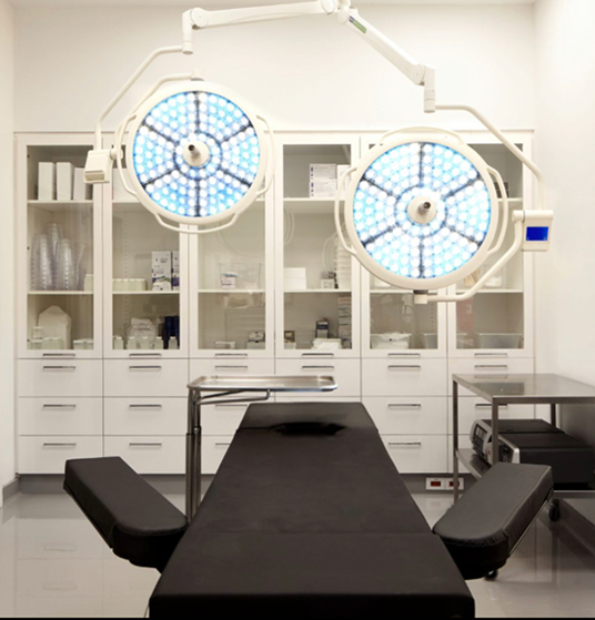 A modern surgical room in Our Practice with an operating table, overhead surgical lights, storage cabinets, and medical supplies.